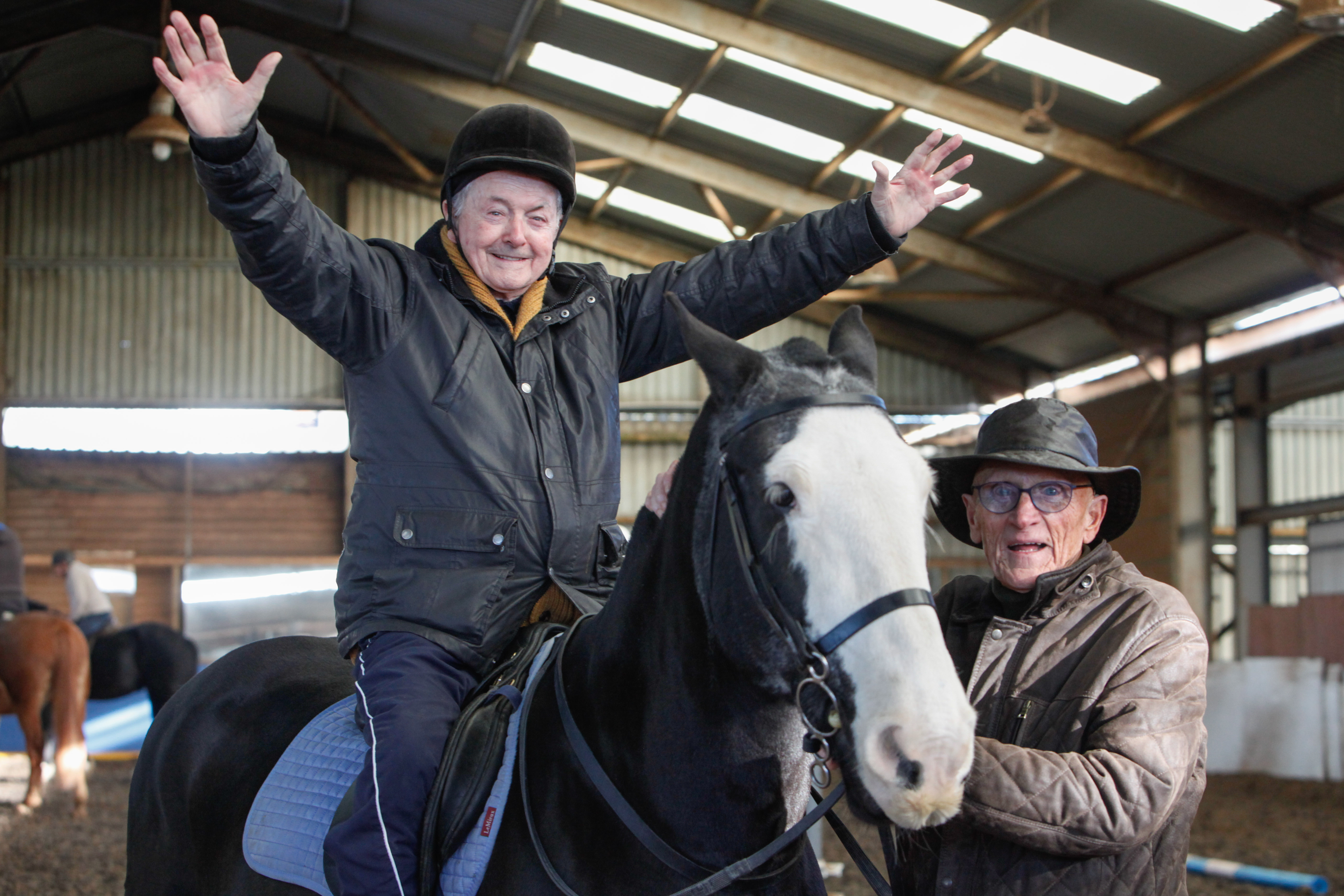 A veteran sits on a horse with arms outstretched while another veteran stands next to them