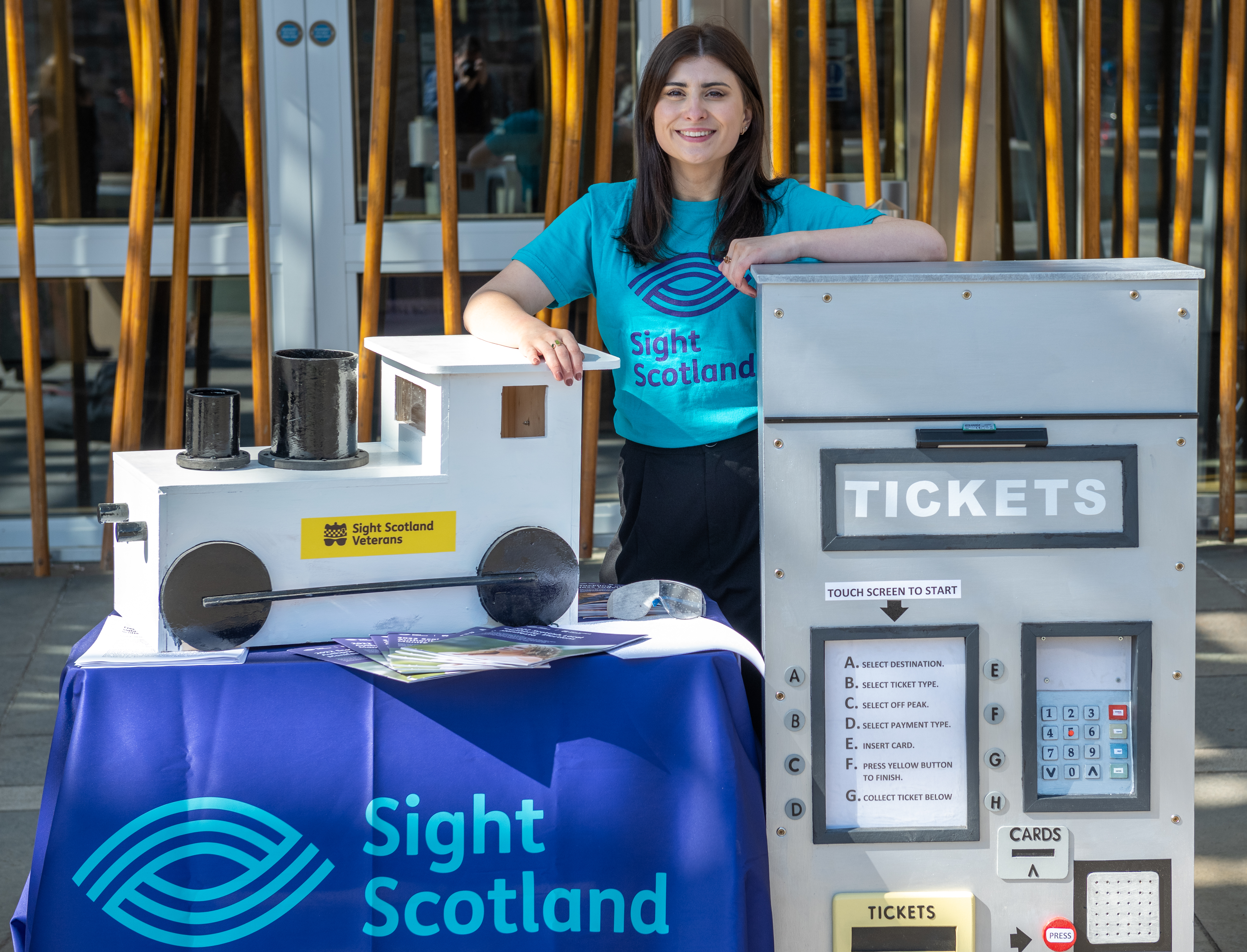sight scotland team member standing behind ticket machine and train prop made for the campaign launch by sight scotland veterans