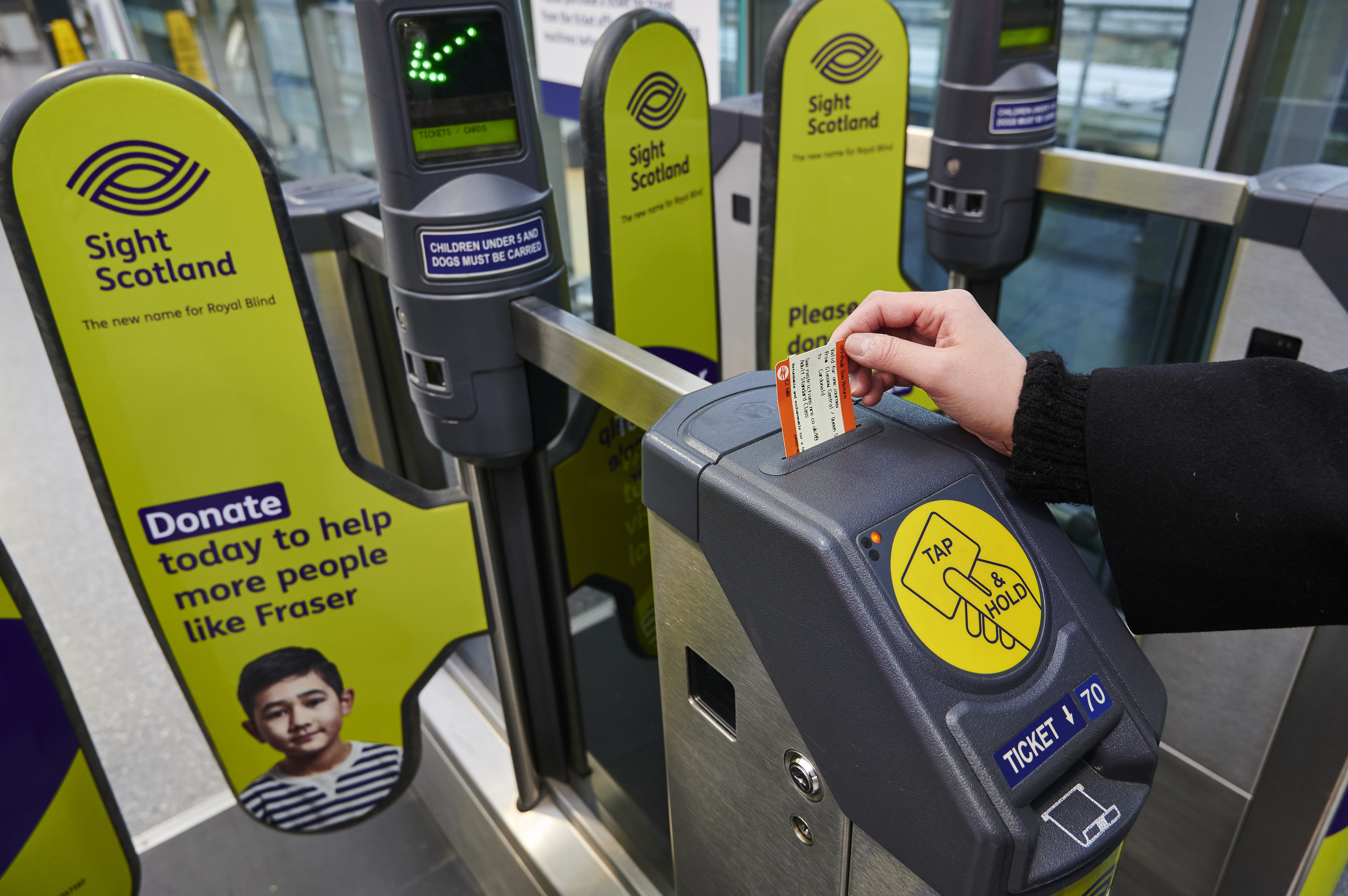 A person with sight loss taking ticket from railway barriers