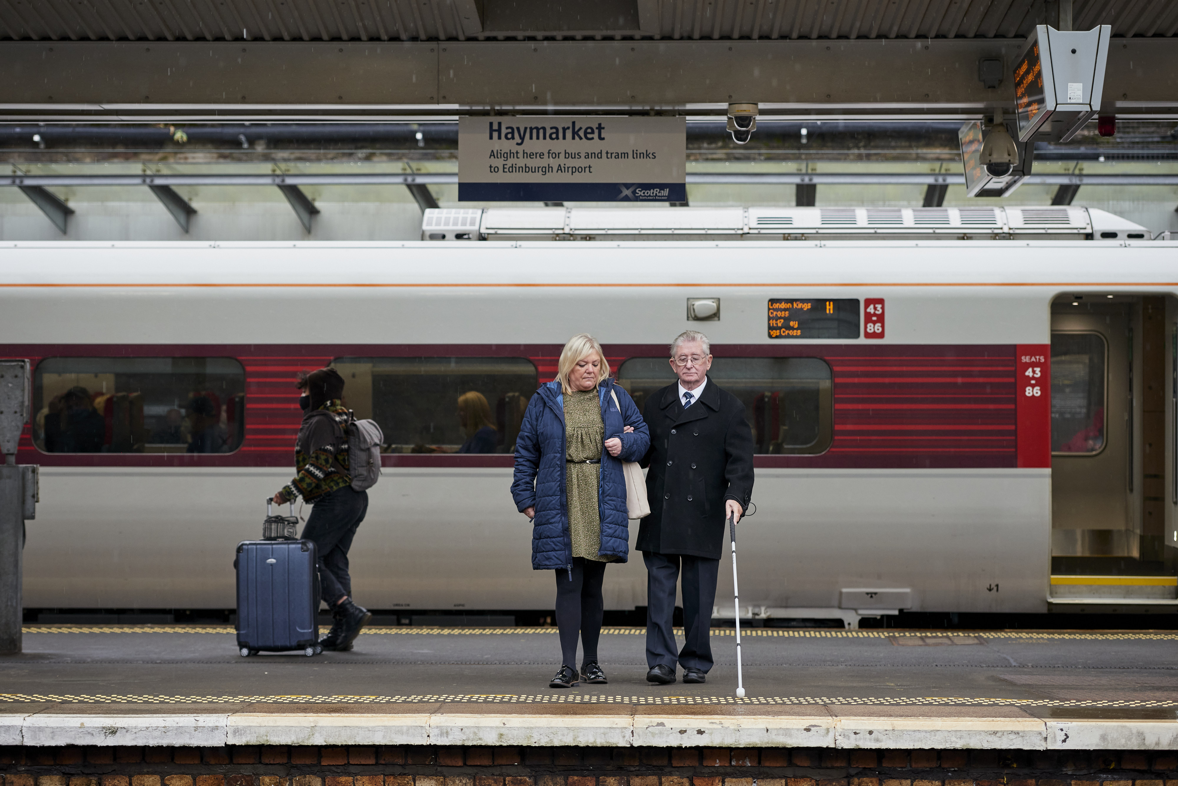 sight scotland veteran and companion waiting on the railway platform with long cane