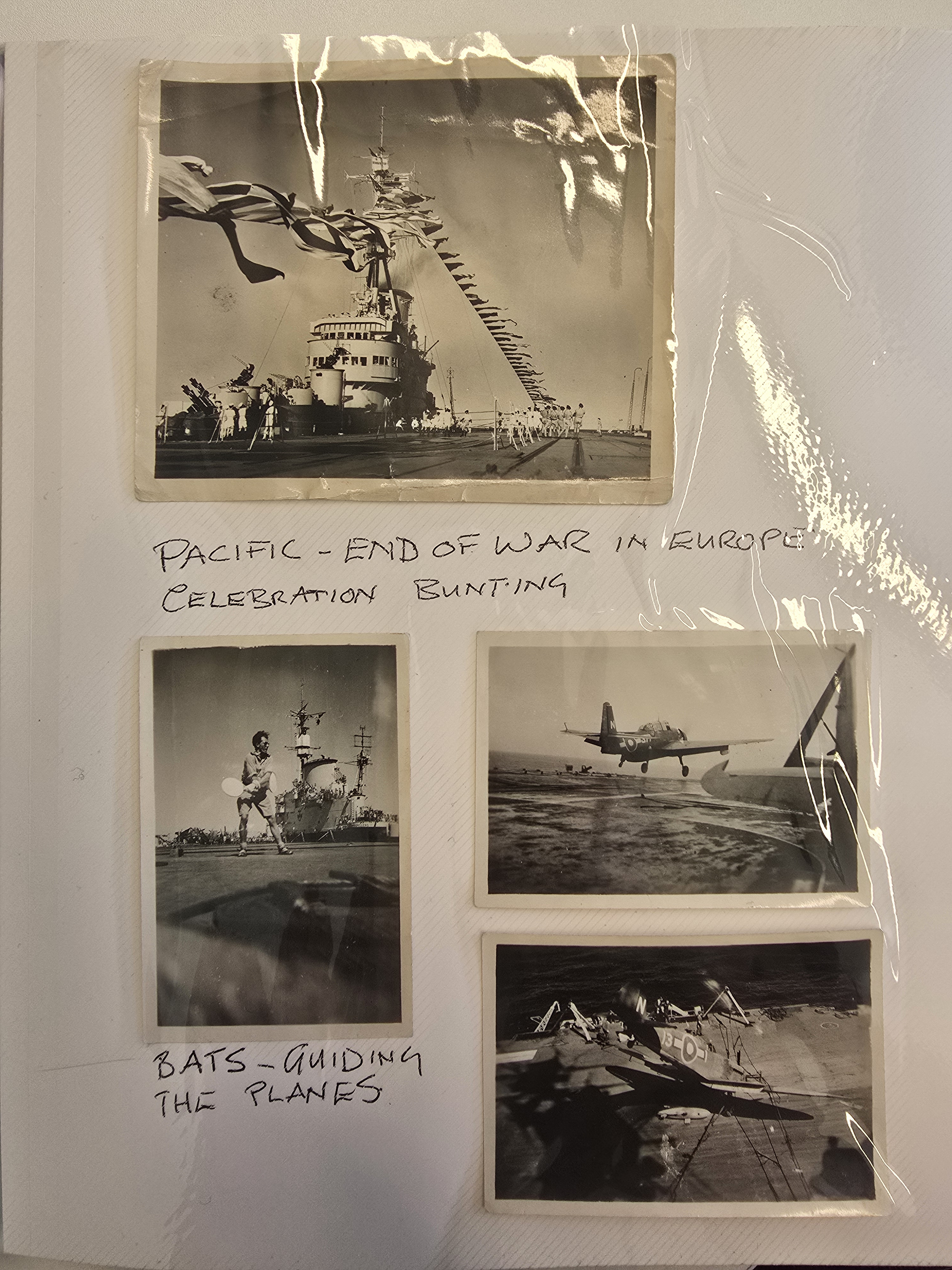 Four black and white photos in a photo album showing a ferry with bunting, a man with white bats guiding a plane to land, and planes taking off. Written beside and beneath them is text reading &quot;Pacific - end of War in Europe celebration bunting&quot; and &quot;Bats - guiding the planes&quot;