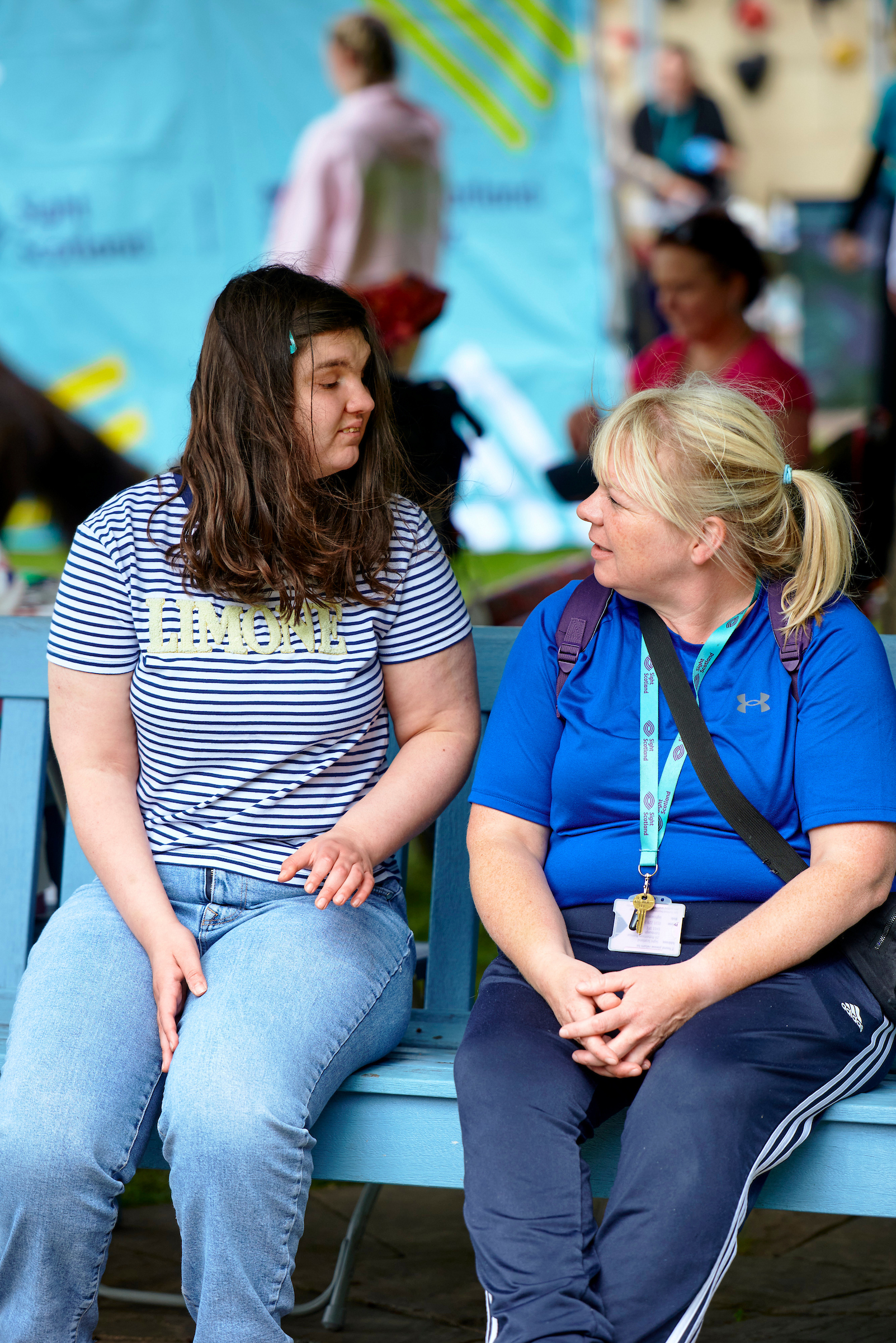 Two woman sit on a blue bench outside