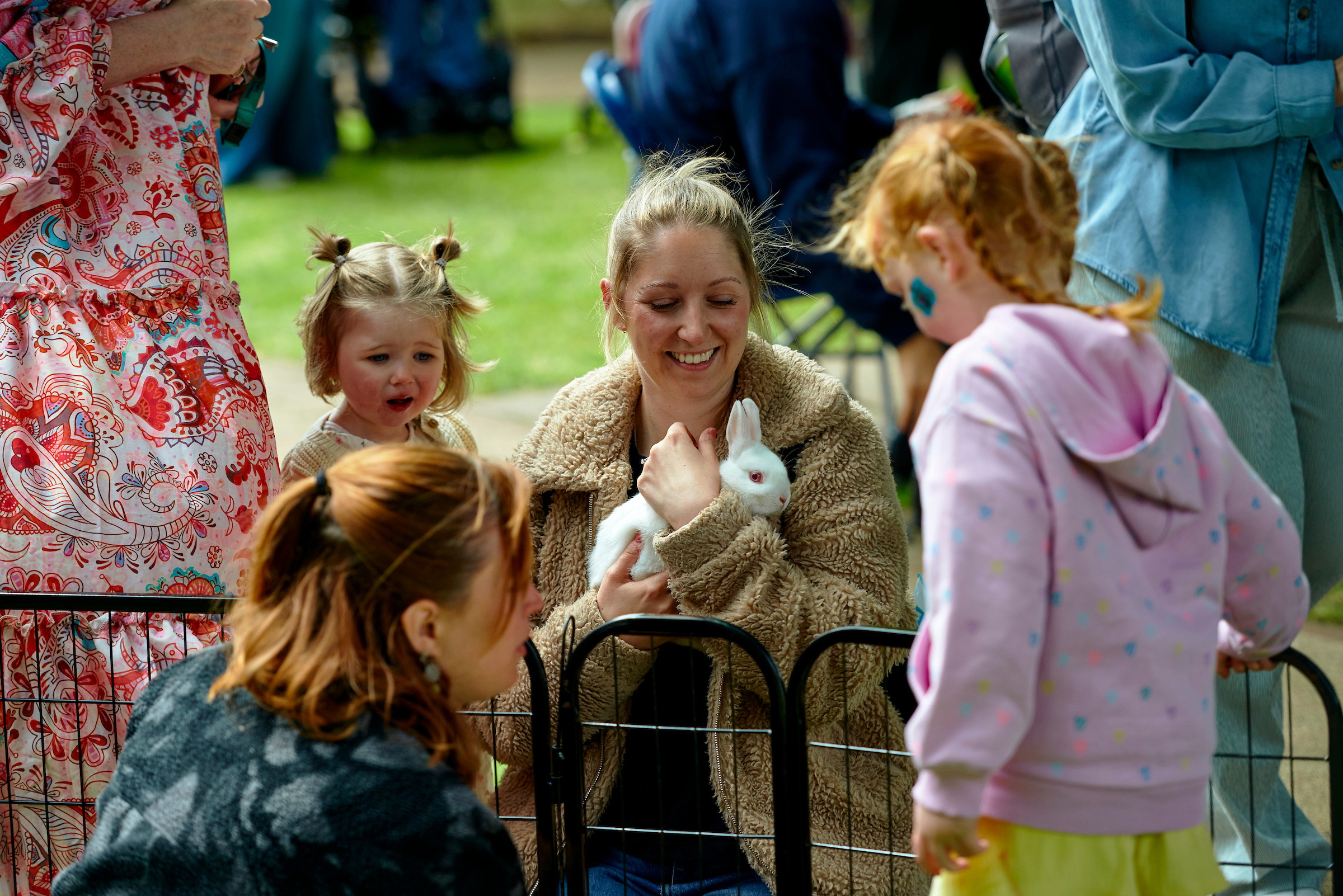 A woman and two young girls crouch near a fence, the woman holding a white rabbit in her arms.