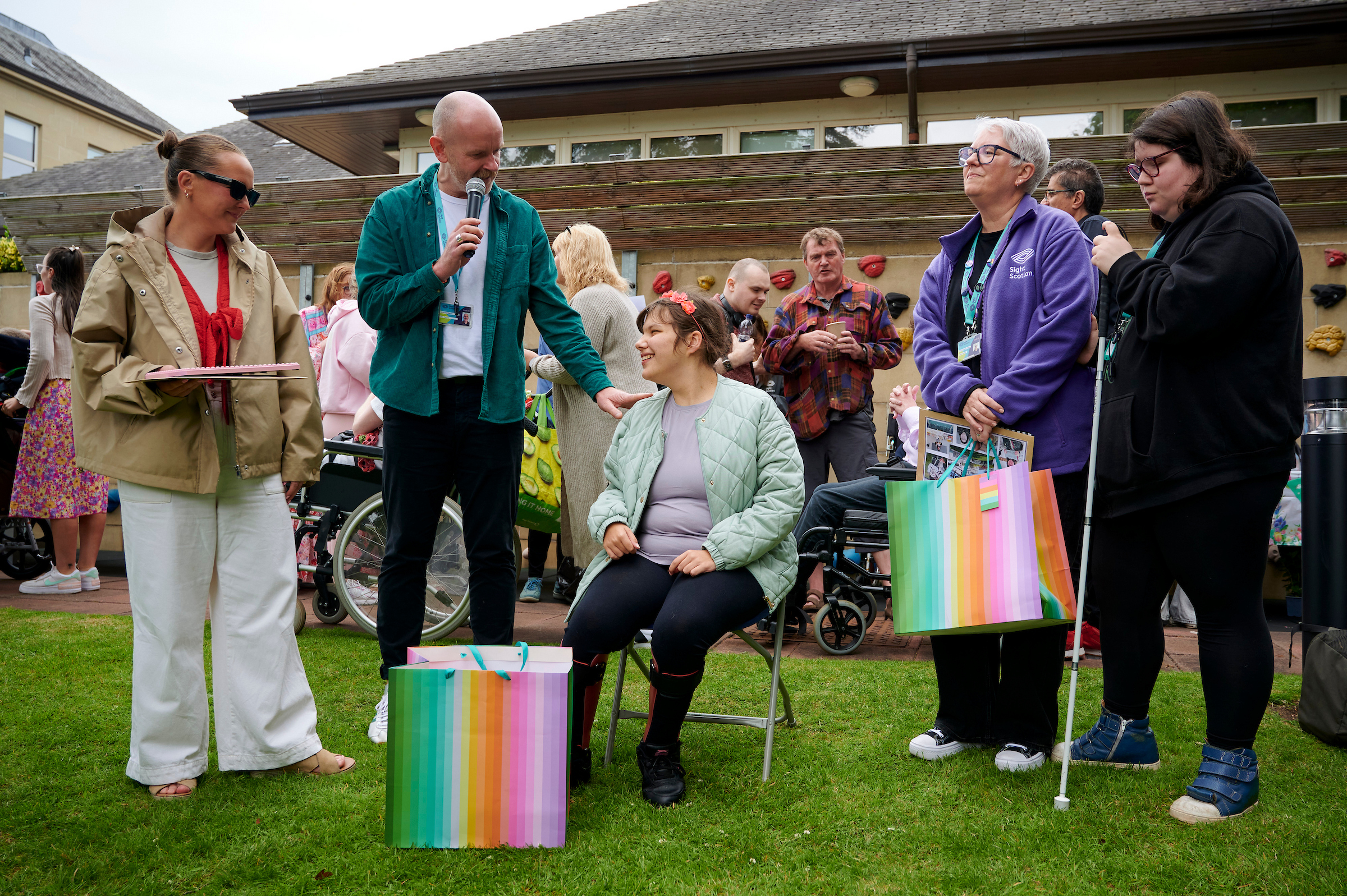 A group of people gather around Rebecca, who sits in the middle, a large gift bag at her feet.