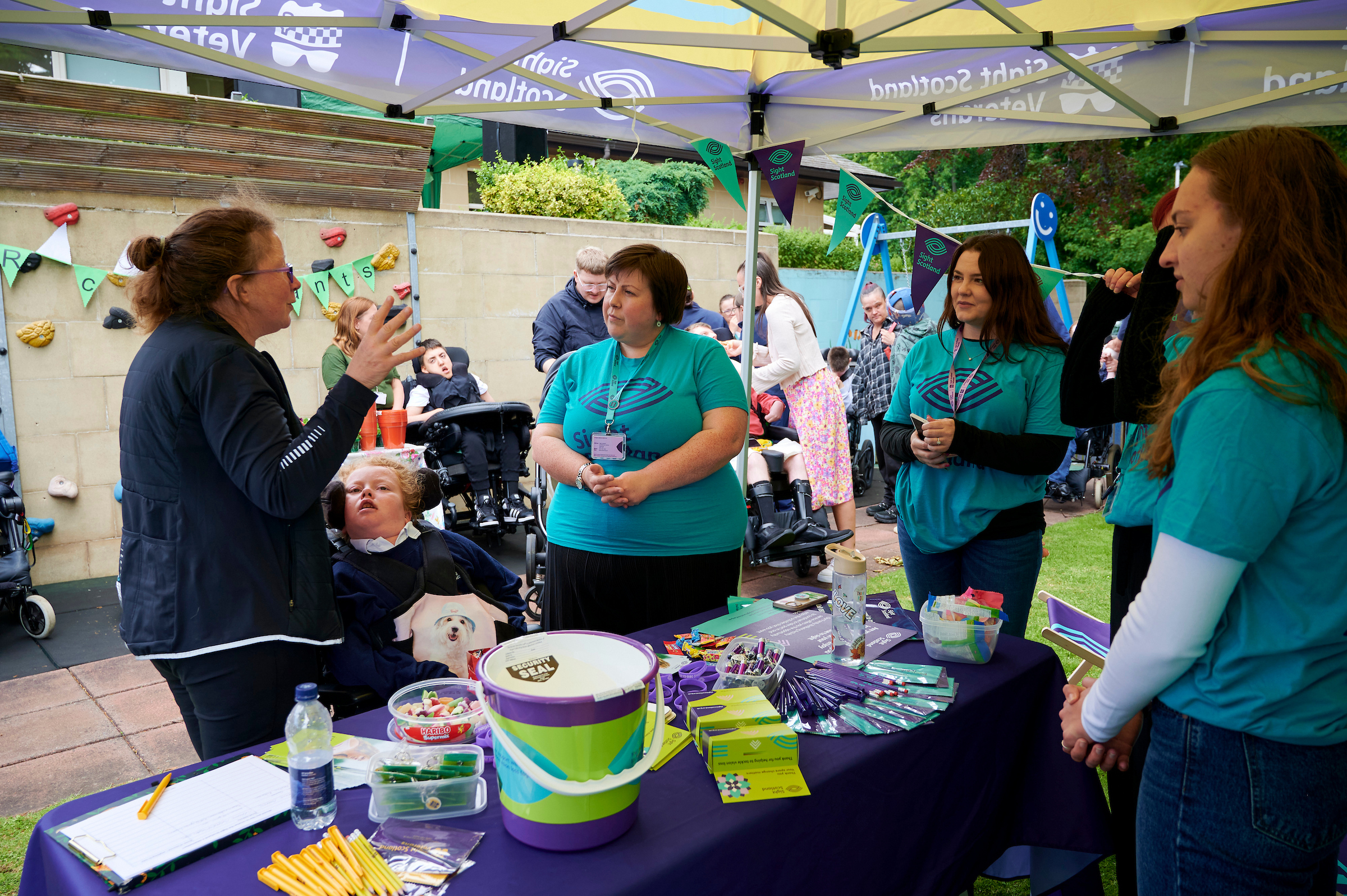 Three women wearing blue Sight Scotland t-shirt stand around a table and converse with another woman.