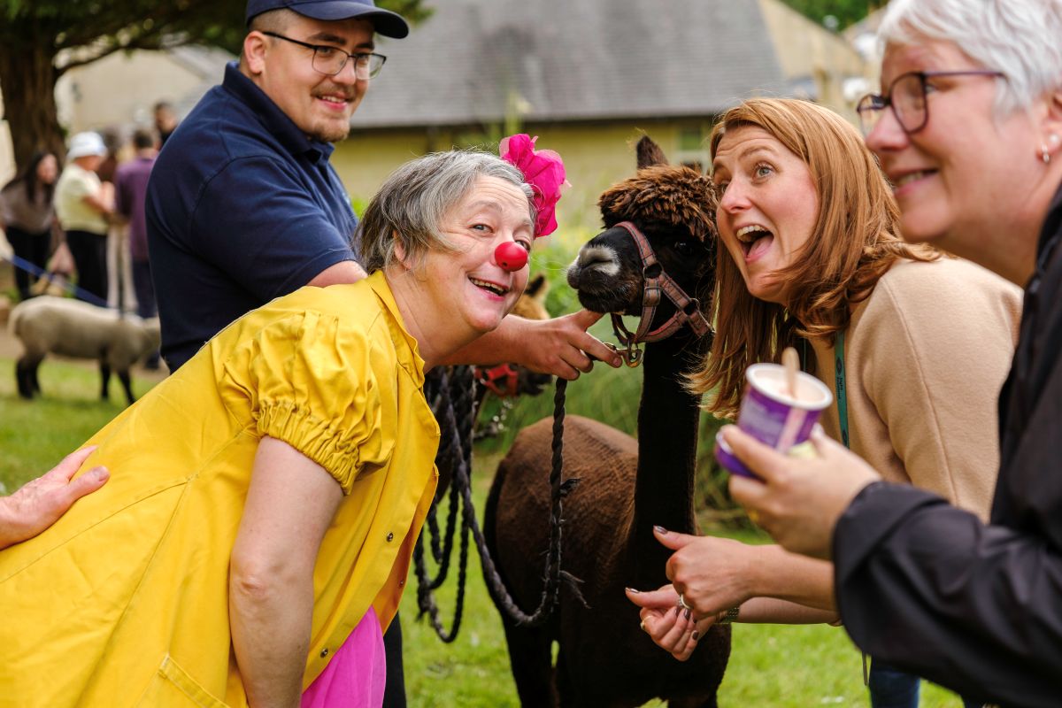 Head of Education Lucy Chetty and a woman dressed as a clown smile and laugh as they pose with an alpaca
