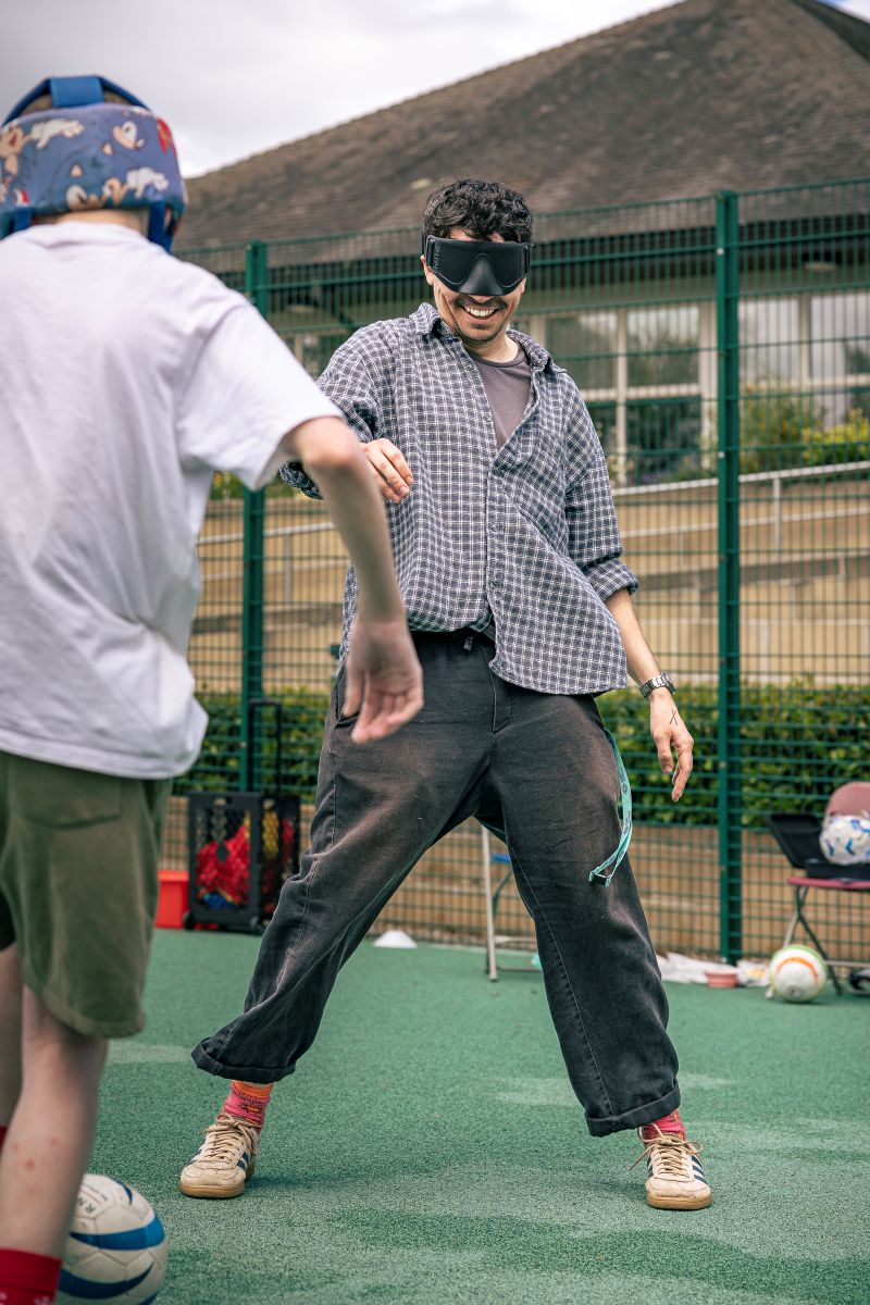A man and a boy play blind football on a pitch, one wears large dark glasses called Sim Specs, at the Royal Blind School Family Fun Day 2026