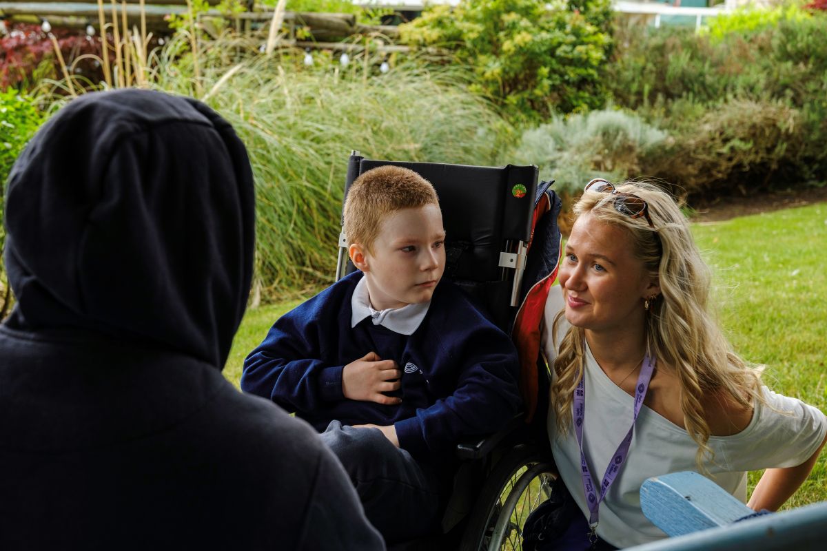 Two people crouched next to a boy in a wheelchair in the gardens at the Royal Blind School Family Fun Day 2026