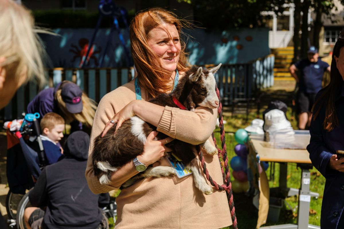 Lucy, Head of Education, stands in the sunshine in the school gardens holding a small goat at the Royal Blind School Family Fun Day 2026