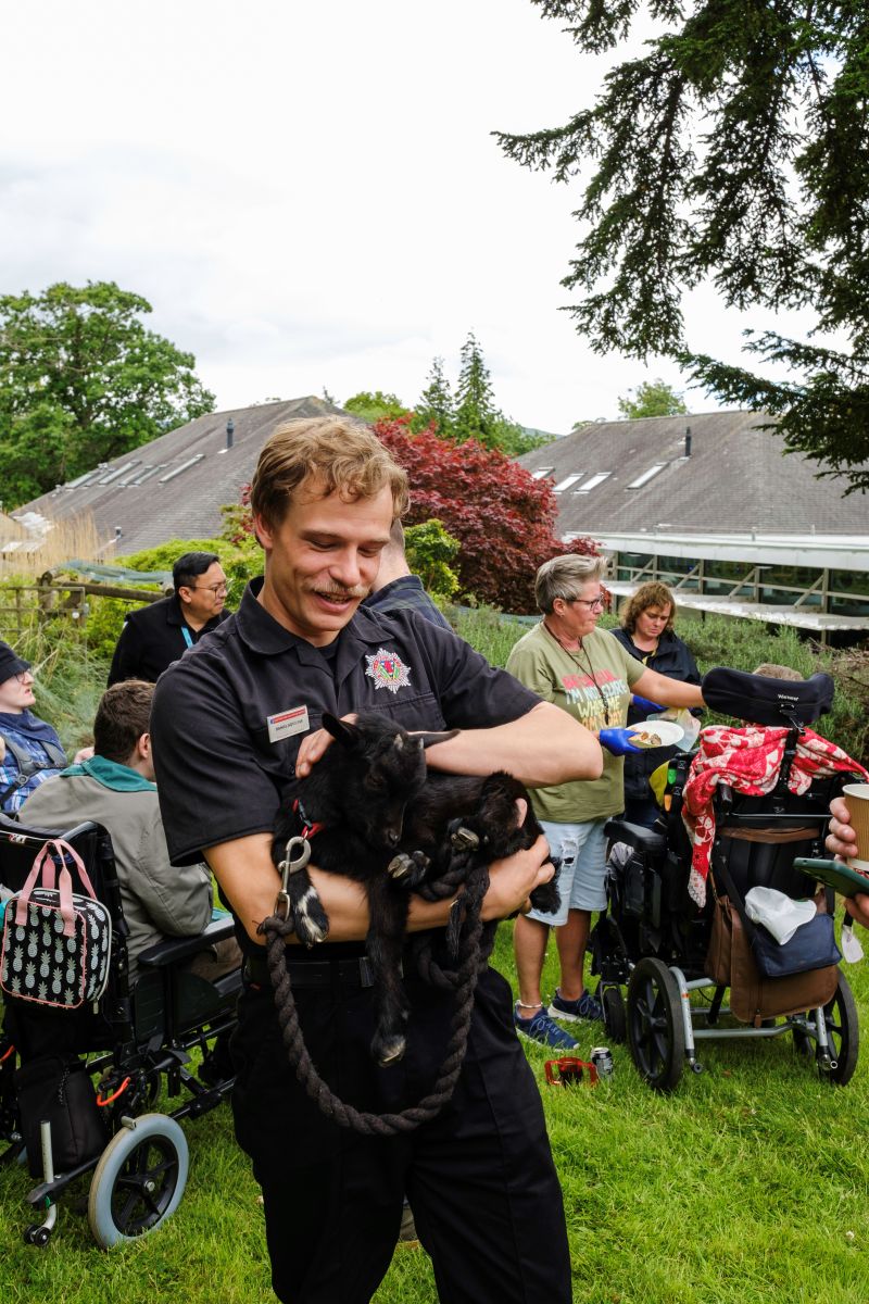 A fireman wearing a uniform holds a small black lamb at the Royal Blind School Family Fun Day 2026