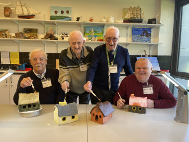 four men smiling at camera with painted clay houses in front of them 