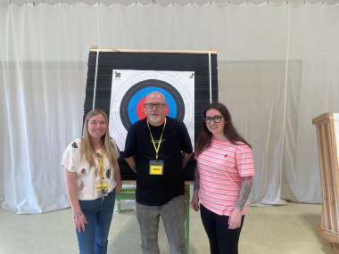 James and Jodie stand in front of a large archery target inside the Linburn Centre, alongside Lyndsey from Sight Scotland Veterans