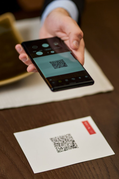 A hand holding a mobile phone above an envelope with a QR code on it, which it is scanning.