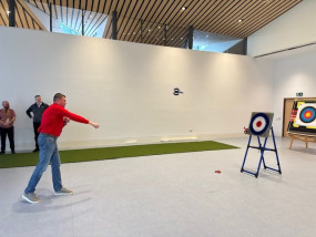 A man in a red jumper throws an object towards a target in a large indoor hall