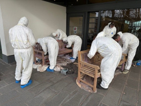 A group of people in white painting suits work on wooden benches outside