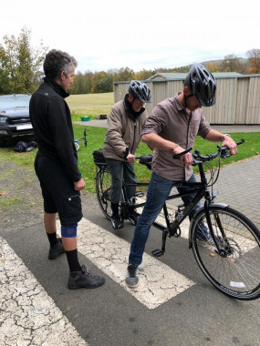 David Glover from Cycling UK stands to the left as Bryce and James mount the tandem bike