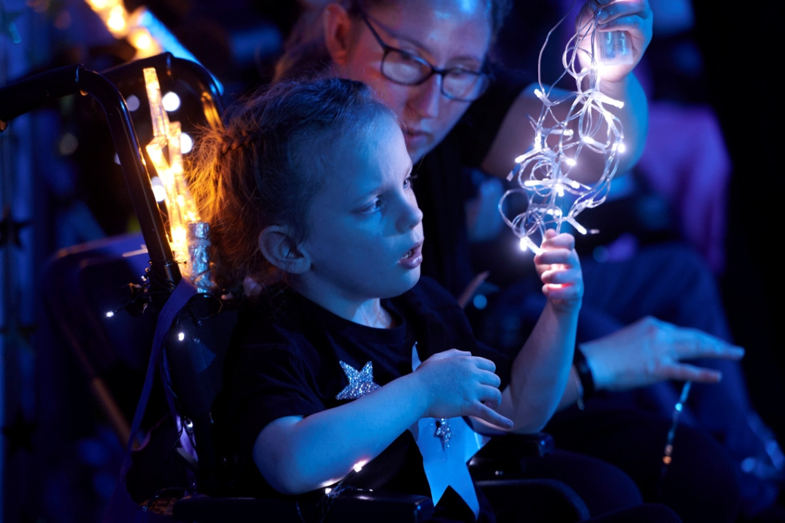 A young girl in a t-shirt with stars adorning it stares entranced at a string of fairy lights held in front of her