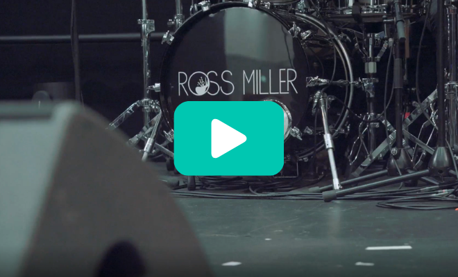 A drum kit with 'ROSS MILLER BAND' written on the front sits on a stage