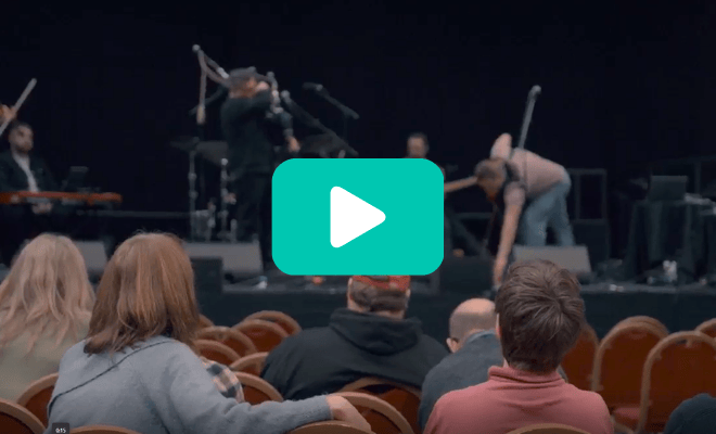 A group of visually impaired Sight Loss Council members sit in front of a stage where musicians are playing