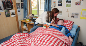 Pupil lies in bed with red checked cover while staff member leans over him