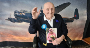 Veteran James Crook waves while holding his birthday card from the Queen
