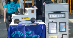 sight scotland team member standing behind ticket machine and train prop made for the campaign launch by sight scotland veterans 