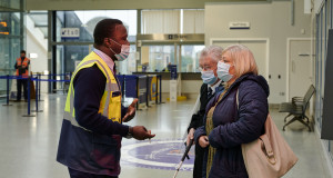 A rail worker assisting a visually impaired person with long cane and their companion in a train station in Scotland