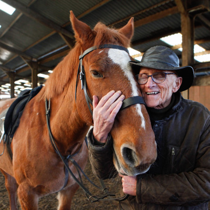 A veteran smiles while hugging a horse on Hawkhead Centre riding activity at Tannoch Stables
