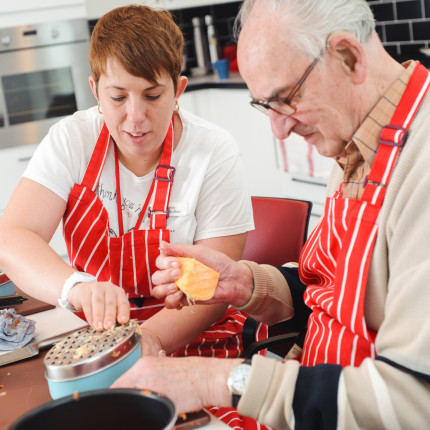 Centre officer helps a veteran with sight loss grate some cheese in the Linburn skills kitchen