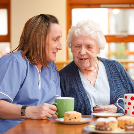 Resident chats with staff member over cakes and tea